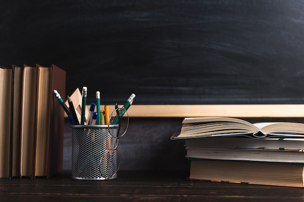 Pennen, potloden, boeken en glazen op tafel, tegen de achtergrond van schoolbord