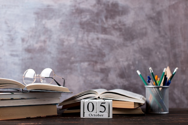 Pens, pencils, books and glasses on the table. Calendar october 5, copy space.