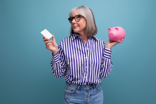 Pension contribution middleaged woman with gray hair holding a piggy bank and a credit card for