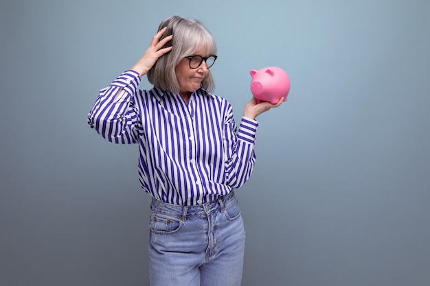 Pension savings a middleaged woman with gray hair holds a piggy bank with money on a bright studio