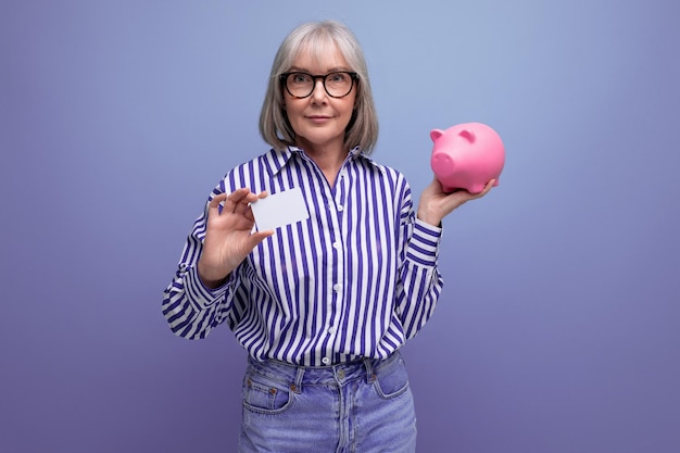 Пенсионные сбережения женщина средних лет с седыми волосами держит копилку с деньгами на яркой студии