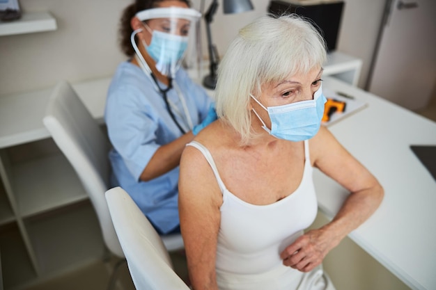 Pensioner having her back listened to with a stethoscope