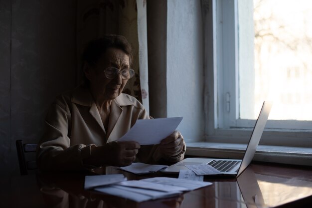 Il pensionato legge innumerevoli giornali ed è molto concentrato. donna maggiore che calcola le tasse a casa. donna in pensione che calcola le sue bollette domestiche. affari, risparmi, assicurazione di rendita, età e concetto di persone