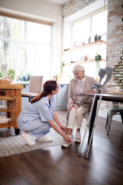 Photo pensioner smiling while caregiver lacing shoes for her