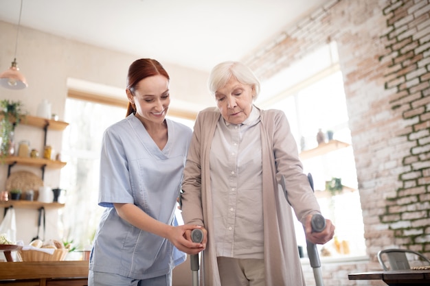 Pensioner walking with crutches standing near caregiver