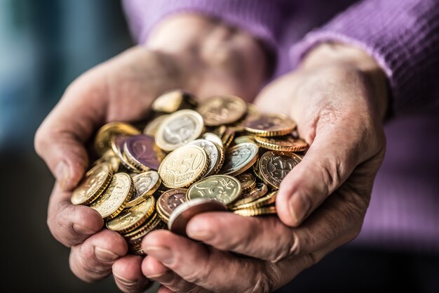 Пенсионерка женщина, держащая в руках монеты евро. Тема низких пенсий.