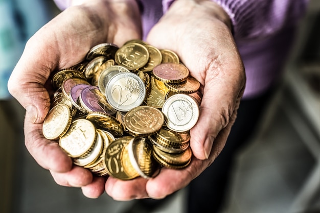 Pensioner woman holding in hands euro coins. Theme of low pensions.