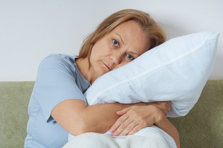 目を開けてソファに座って、枕を抱きしめて、不眠症に苦しんでいる年金受給者の女性。