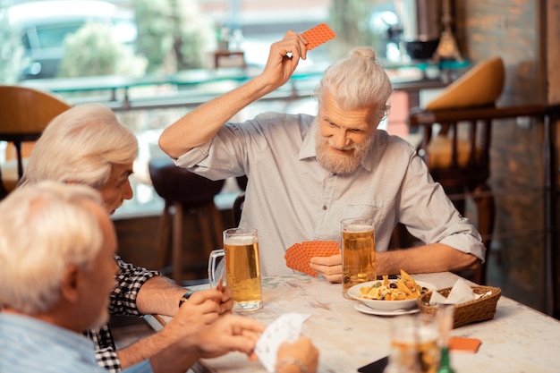 Pensioners playing cards. Grey-haired positive pensioners playing cards and drinking