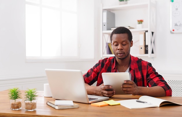 Pensive african-american businessman in office working with laptop and digital tablet, copy space