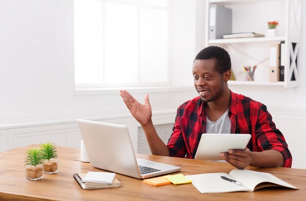 Задумчивый афро-американский бизнесмен в офисе, работая с ноутбуком и цифровым планшетом, копией пространства