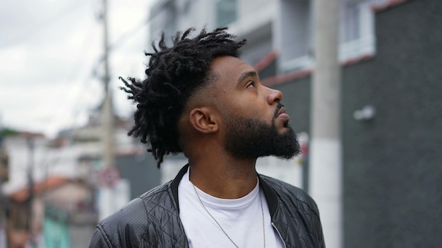 A pensive African American man looking up to sky in contemplation standing by urban street