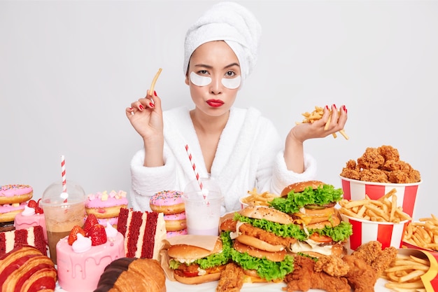 Pensive Asian woman focused at camera surrounded by fast food