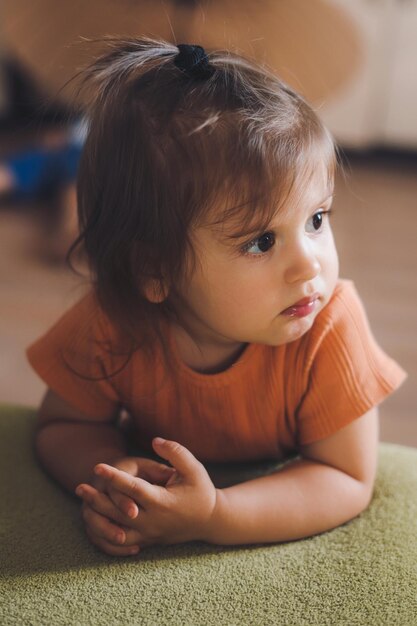 Pensive baby girl sitting on floor leaning on the sofa in living room Eye care Beautiful girl portrait Carefree childhood