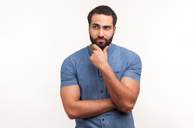 Pensive bearded man holding chin with hand need to think planning strategy thinking over ideas for startup Indoor studio shot isolated on white background