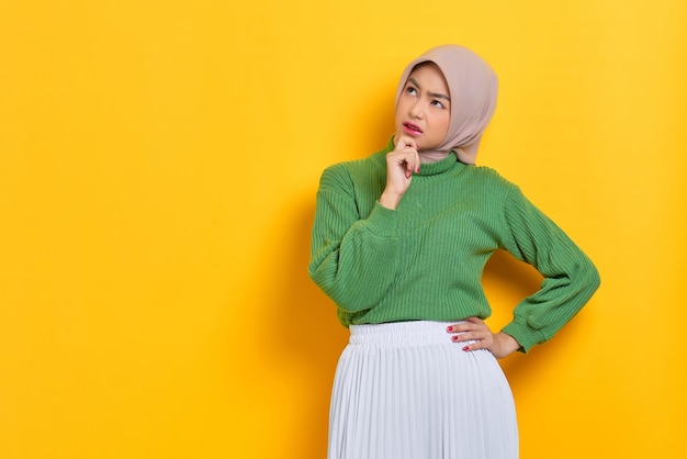 Pensive beautiful asian woman in green sweater thinking about something and looking away isolated over white background