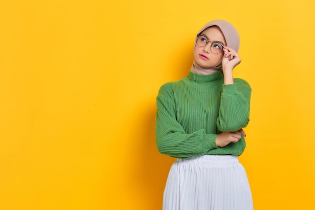 Pensive beautiful Asian woman in green sweater thinking about something and looking away isolated over white background