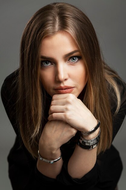 Pensive beautiful woman. Beautiful blonde in a black shirt. Gray background. Vertical.