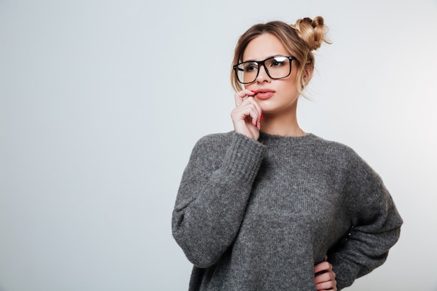 Pensive beautiful young woman in glasses standing and thinking