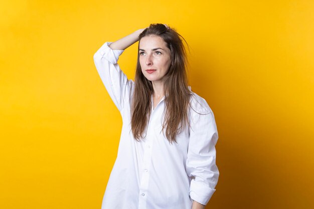 Pensive beautiful young woman in a white shirt on a yellow background