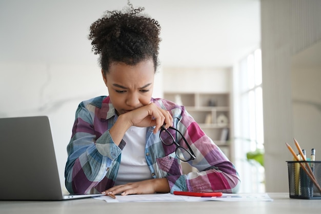 pensive biracial student diligently prepares for exams studying at home desk tired yet focused engaged in distance education