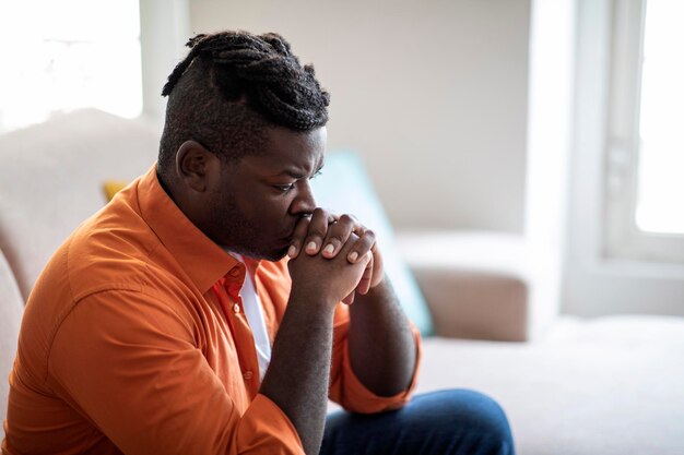 pensive black man sitting on couch at home copy space
