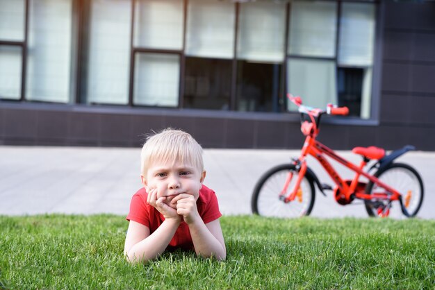 物思いにふける金髪の少年が芝生の上で休んでいます