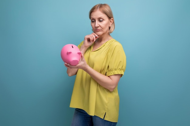 Pensive blond middleaged woman holding a piggy bank in her hands