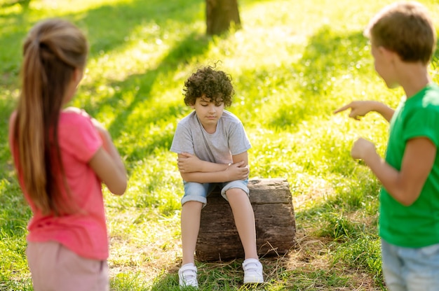 Pensive boy sitting on tree stump and friends