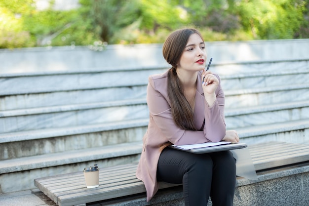 Задумчивая деловая женщина, сидящая на скамейке в парке