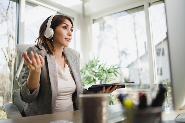 A pensive business woman with headphones using a computer to have a web conference at home office.