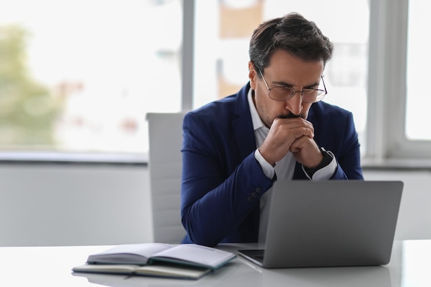 Pensive businessman in blue suit deeply focused on his laptop screen