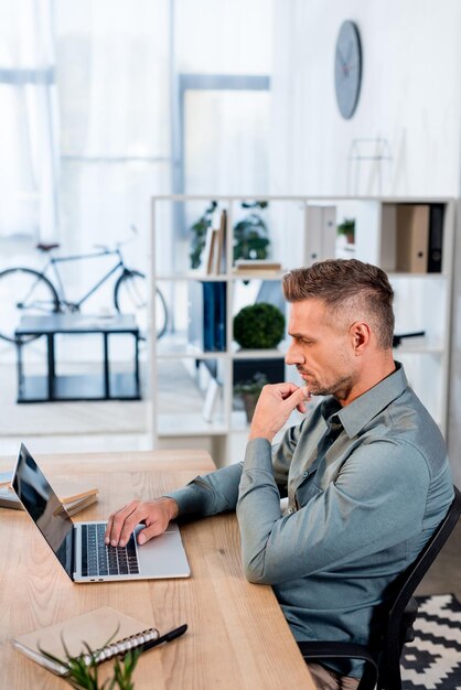 Pensive businessman looking at laptop while sitting in modern office