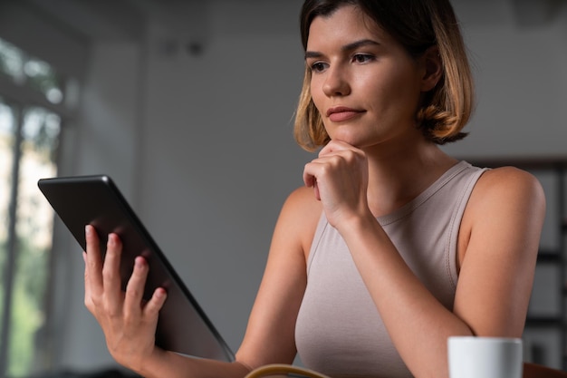 Pensive businesswoman in casual wear holding tablet device touching chin