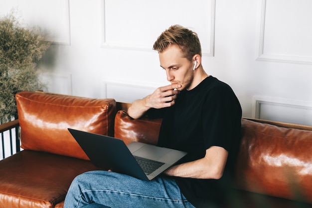 Pensive caucasian man mobile developer programmer writes program code on a laptop computer in home office.