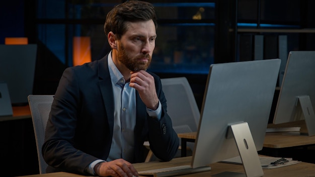 pensive caucasian middleaged man sit at night office thinking deep thought dreaming new project