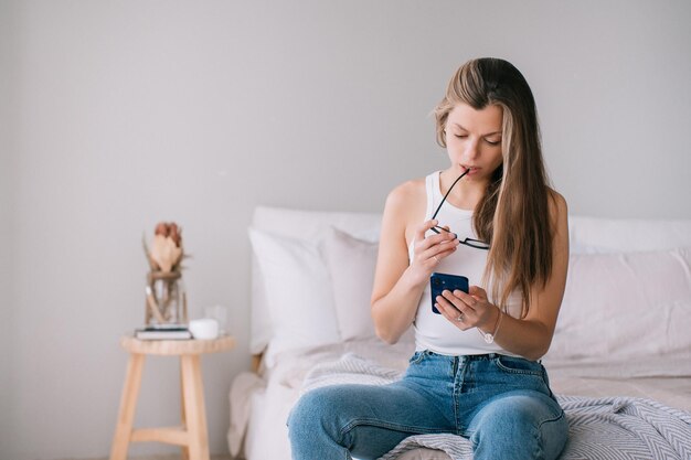 Pensive caucasian young adult woman in blue jeans and white tshirt holds phone reads unexpected