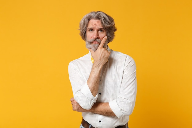 Pensive displeased elderly gray-haired mustache bearded man in white shirt bow tie posing isolated on yellow orange background. People lifestyle concept. Mock up copy space. Put hand prop up on chin.