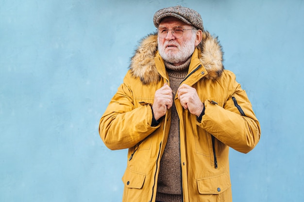 Foto uomo barbuto anziano pensieroso che afferra cappotto alla moda e distoglie lo sguardo. uomo anziano in tuta sportiva gialla