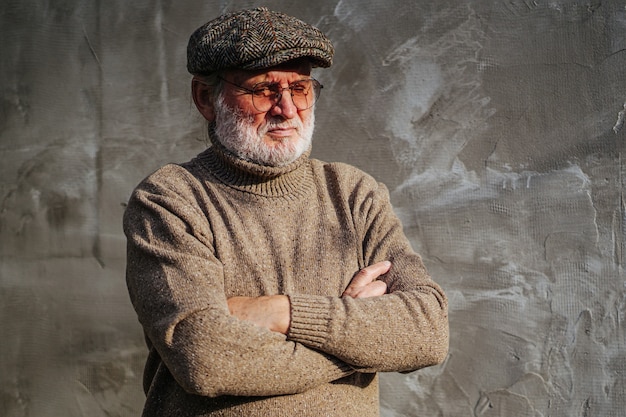 Photo pensive elderly male in stylish knitted sweater and cap crossing arms