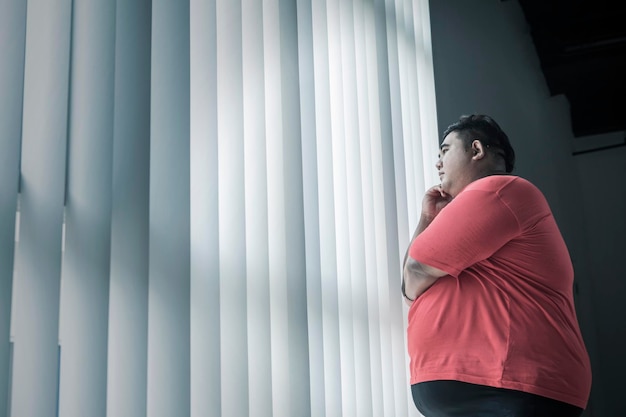 窓の外を見て物思いにふけるデブ男