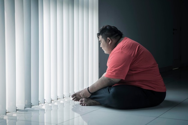 Pensive fat man sitting near the window