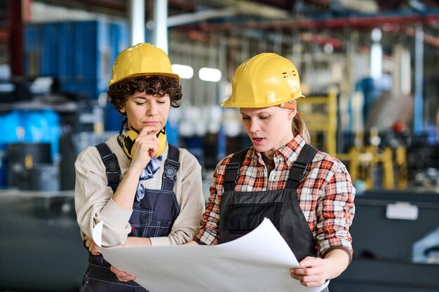 Pensive female engineer looking at sketch on blueprint held by colleague