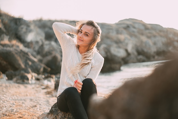 Pensive girl in sweater and pants on the background of the sea and rocks