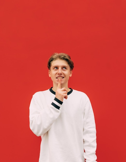 Pensive guy in casual clothes stands on a background of a red wall