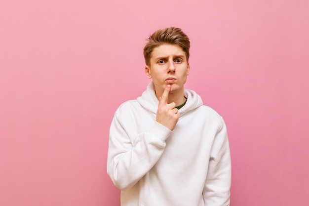 Pensive guy in casual clothing on a pink background looks into the camera with a serious face