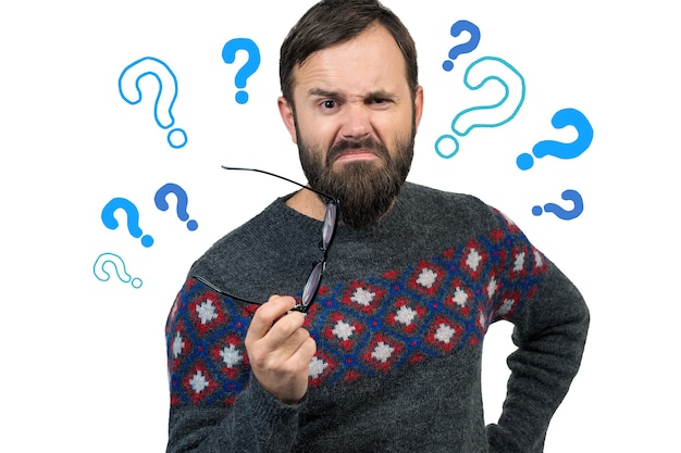 Photo a pensive guy with a beard and glasses on a white background with question marks ponders what to do