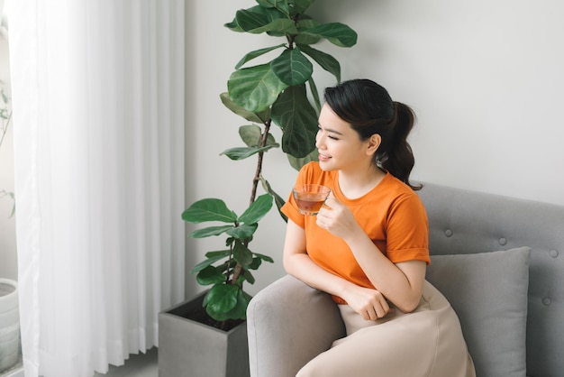 Pensive lady holding a cup of tea sitting on a couch in the\
living room at home