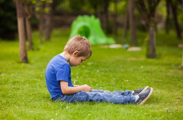 The pensive little boy is sitting on the green grass