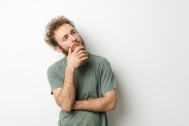 Pensive look of a handsome young man with curly hair in olive t-shirt looking upwards